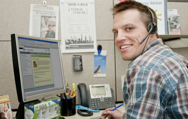 Настольный компьютерный монитор, человек с ручкой, наушники и человек за столом.