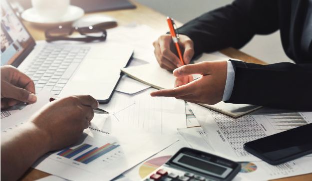 Мужчина пишет на ноутбуке текст с помощью ручки, рядом с мобильным телефоном.