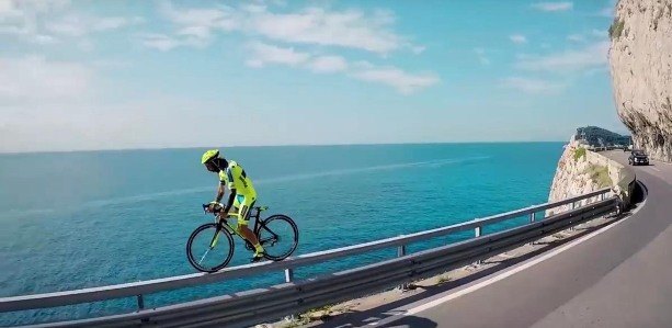 Велосипедист в шлеме на фоне автомобиля, одетый в специальную одежду и обувь.