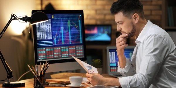 Мужчина с кружкой кофе перед монитором, лицо в камеру.