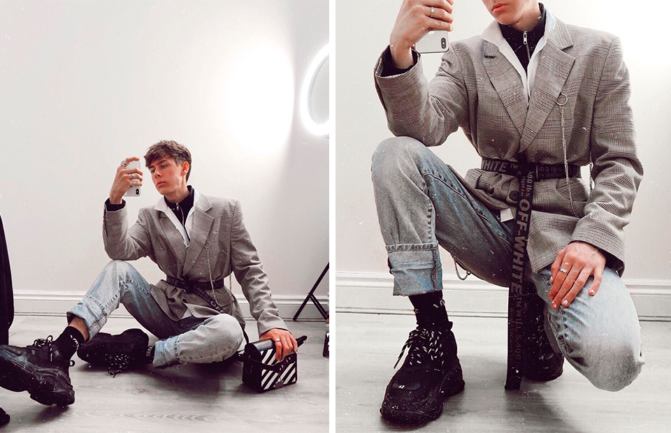 Мужчина в кроссовках и пиджаке сидит, рядом с ним пара брюк и обувь.