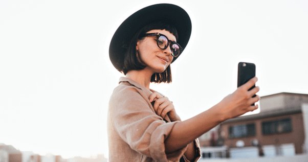 Фотография женщины в шляпе, делающей селфи, изображены лицо и голова.