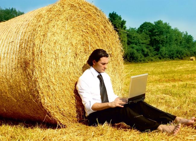 Подросток парень, сидящий на соломе с ноутбуком, в природе.