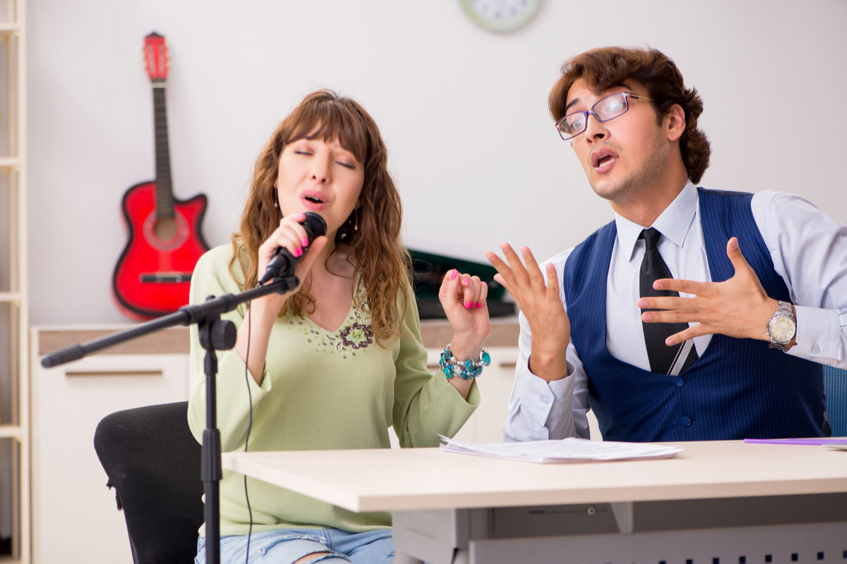 Человек-мужчина с гитарой и микрофоном, носит галстук и очки, крупный план лица.