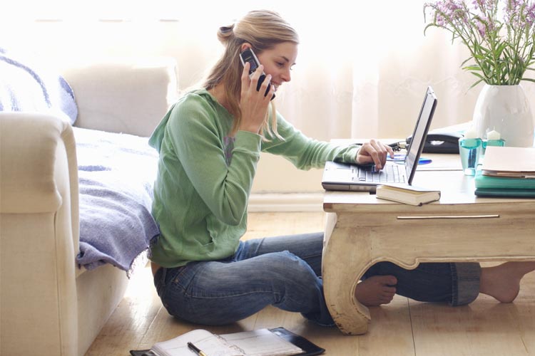 Человек сидит с открытой книгой, лэптопом, мобильным телефоном, ручкой и чашкой.