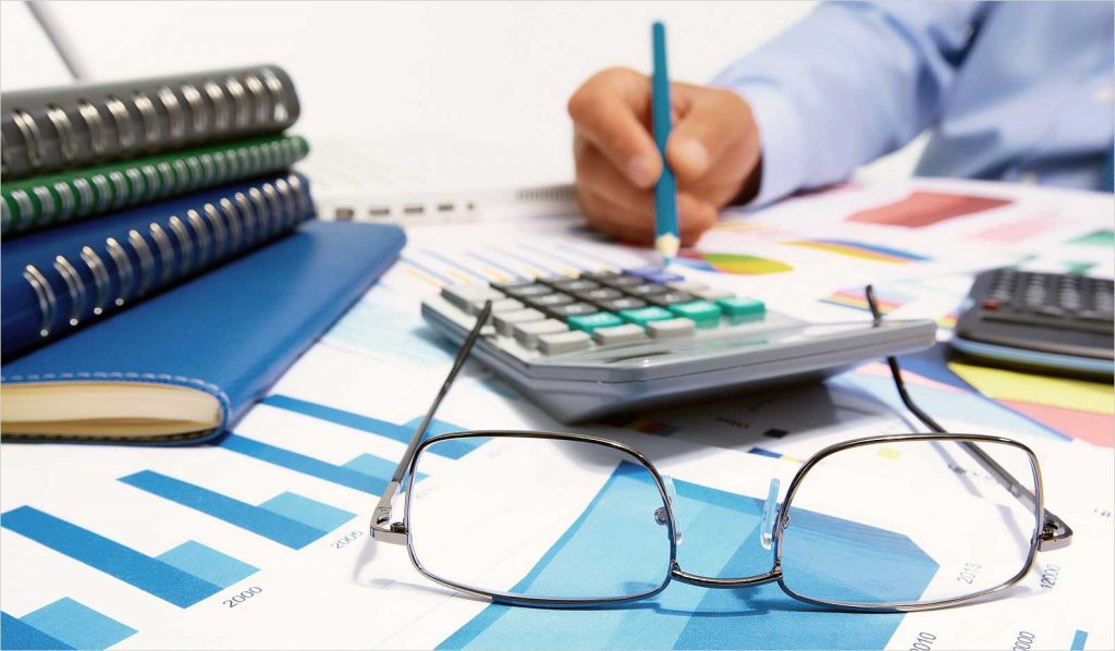 Человек со стильными очками пишет ручкой, окруженный аксессуарами в кадре.