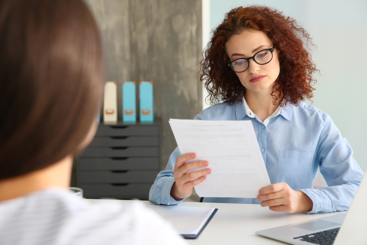 Беседа женщины на собеседовании с документами и ноутбуком в заголовке.