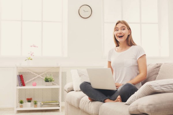 Женщина взяла на ладони ноутбук, счастливо улыбается рядом с растением.