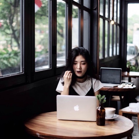 Человек с черными волосами, работающий на ноутбуке, возле автомобиля с чашкой кофе.