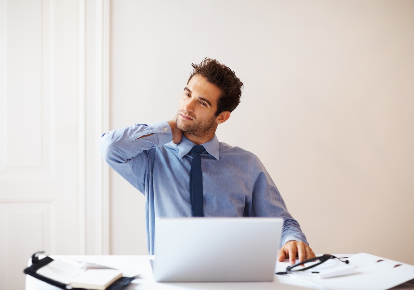 Взрослый мужчина в рубашке с галстуком работает за ноутбуком, держит голову.