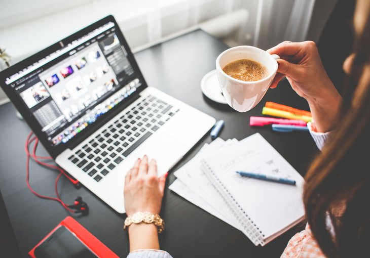 Компьютерная клавиатура, ноутбук, монитор, кружка кофе, ручка на рабочем столе.