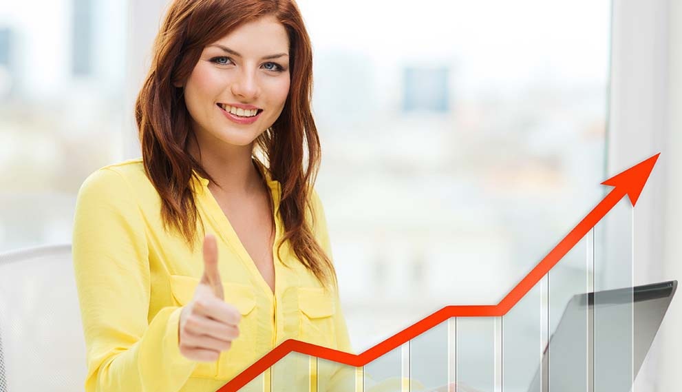 Женщина с улыбкой, в пальто, прикасается к лицу пальцем.