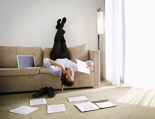 Мужчина на диване с ноутбуком, кроссовками и перчатками для пилатеса.