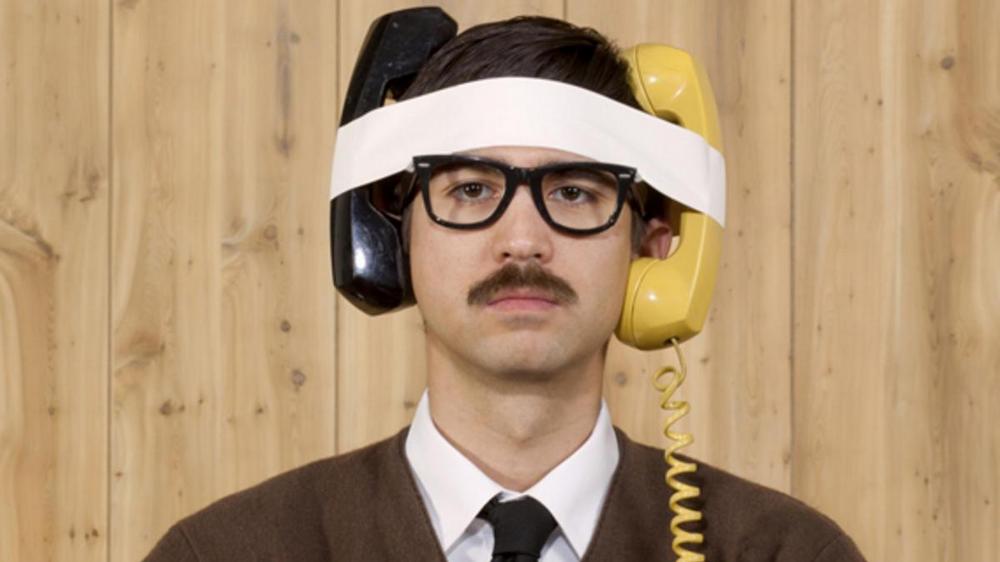 Мужчина в костюме и очках с каской, глядящий камере.