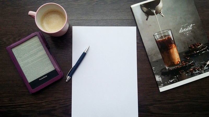 Рабочий стол с компьютером, телефоном, планшетом, ручкой и чашкой на фоне мебели.