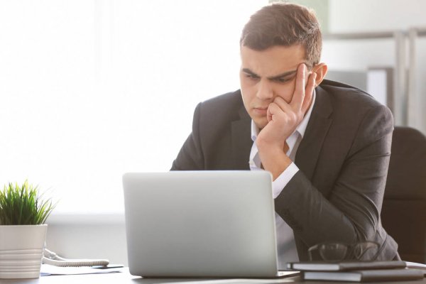 Мужчина в костюме с грустным лицом за ноутбуком около растения.