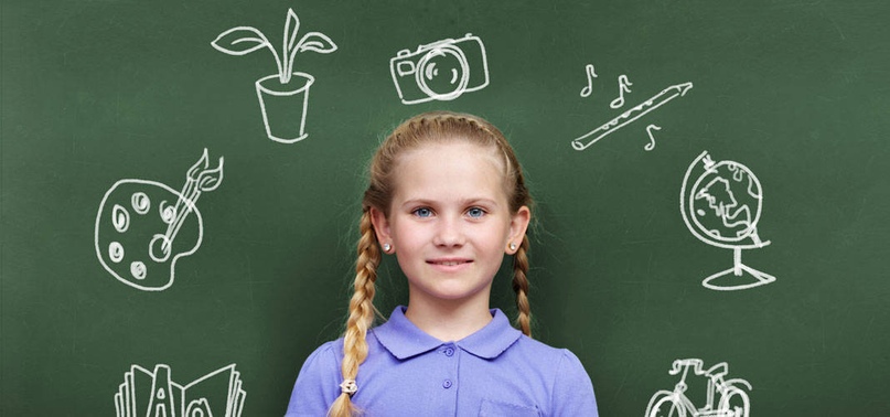 Девочка с косичками, стоящая перед доской с текстом.