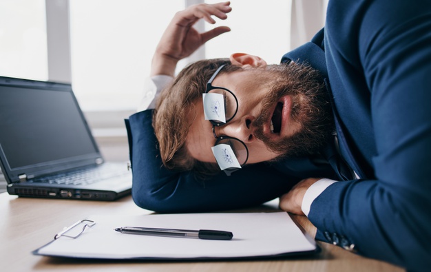 Мужчина с ручкой и ноутбуком, сидит за монитором с чашкой.