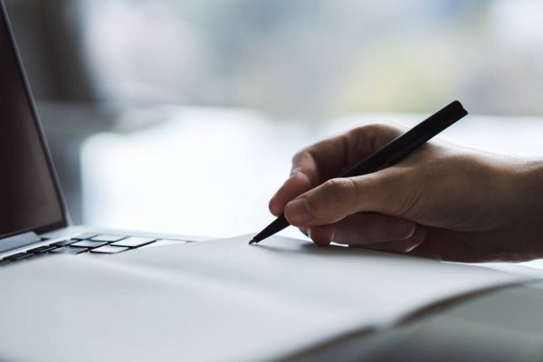 Человек пишет на ноутбуке с использованием пера, компьютер и электроника вокруг.