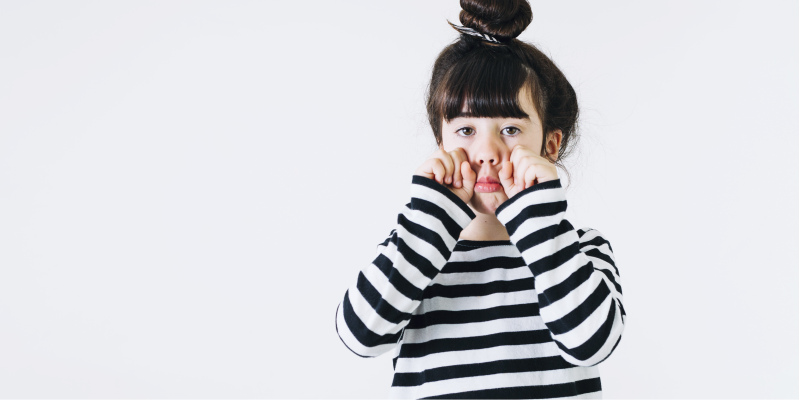 Фотография портрета девочки с выразительным лицом, держащей пальчик рядом с лицом.