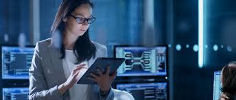 "Person reading on tablet computer, wearing coat, surrounded by electronics and computer."