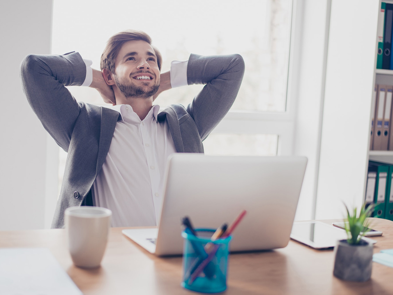 Голова счастливого мужчины, работающего за ноутбуком, с триумфом удерживая кофейную чашку.