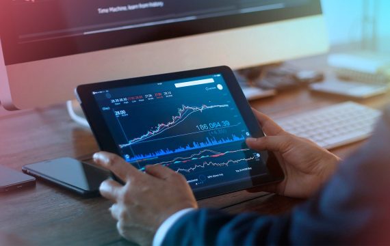 Человек использует планшет и мобильный телефон на фоне компьютерной клавиатуры.