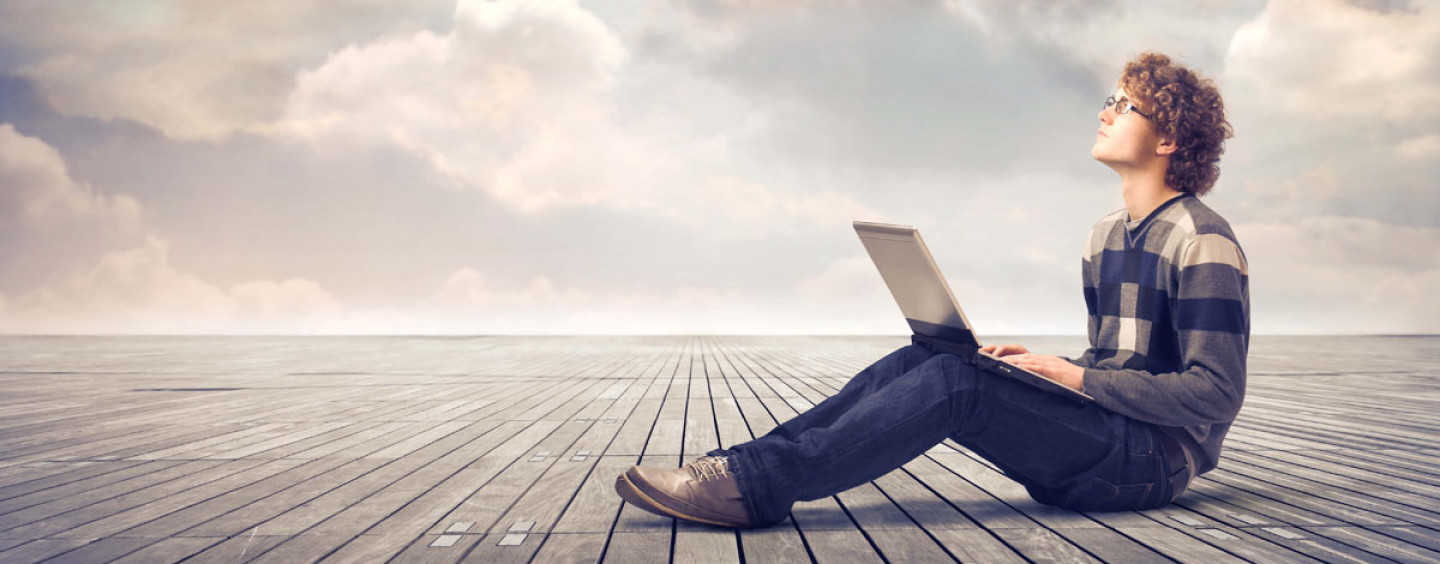 Подросток-мужчина сидит за ноутбуком в джинсах и кроссовках, выполняя фотосъемку.