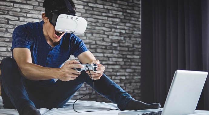 Фотография человека в VR-гарнитуре, играющего в видеоигры на ноутбуке и ПК.