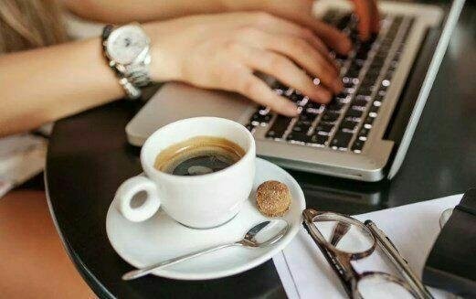 "Ноутбук на столе с чашкой кофе, электроника и мебель, офисная атмосфера."