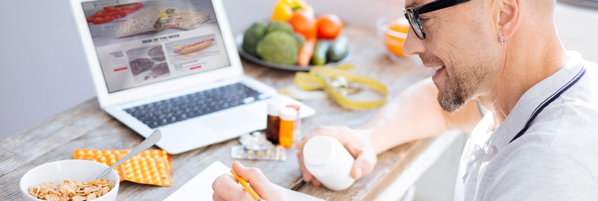 Мужчина с очками, работающий на ноутбуке, завтракает в столовой с чашкой для каши.