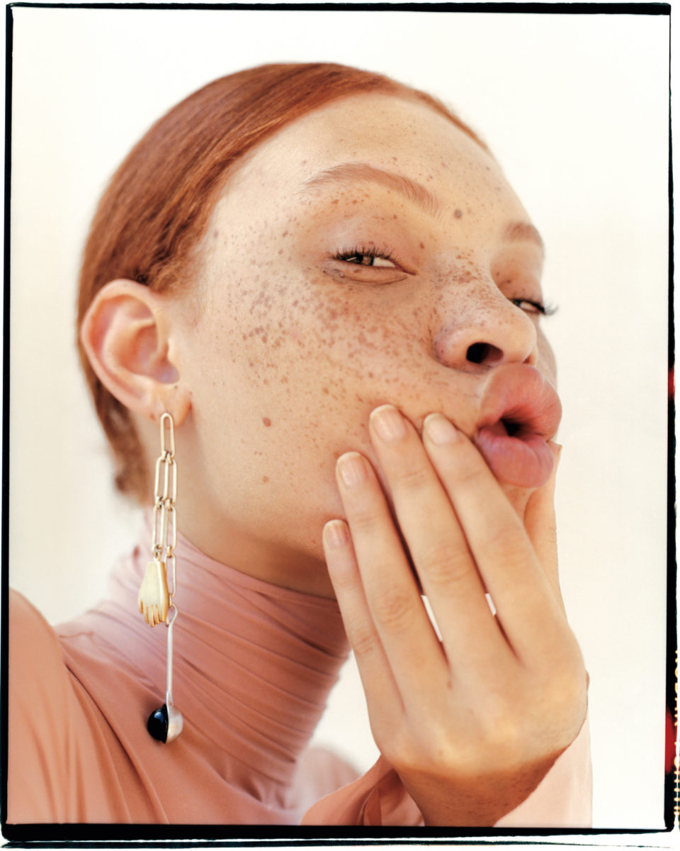 Женщина с веснушками и серьгой, держащая палец у лица на портрете.