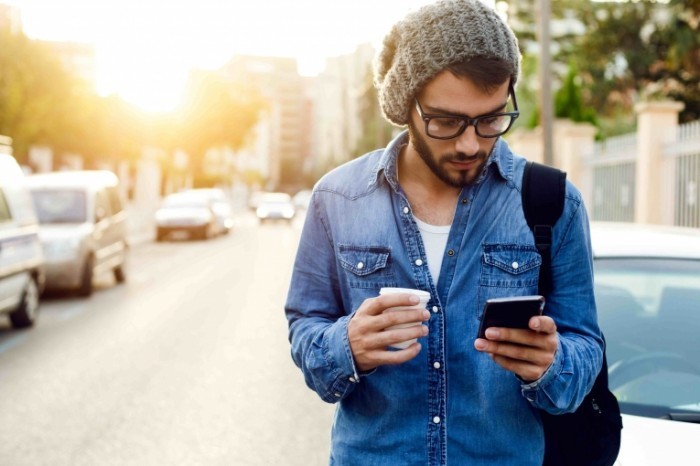 Мужчина смеется, держа телефон и кофейный стаканчик возле автомобиля.