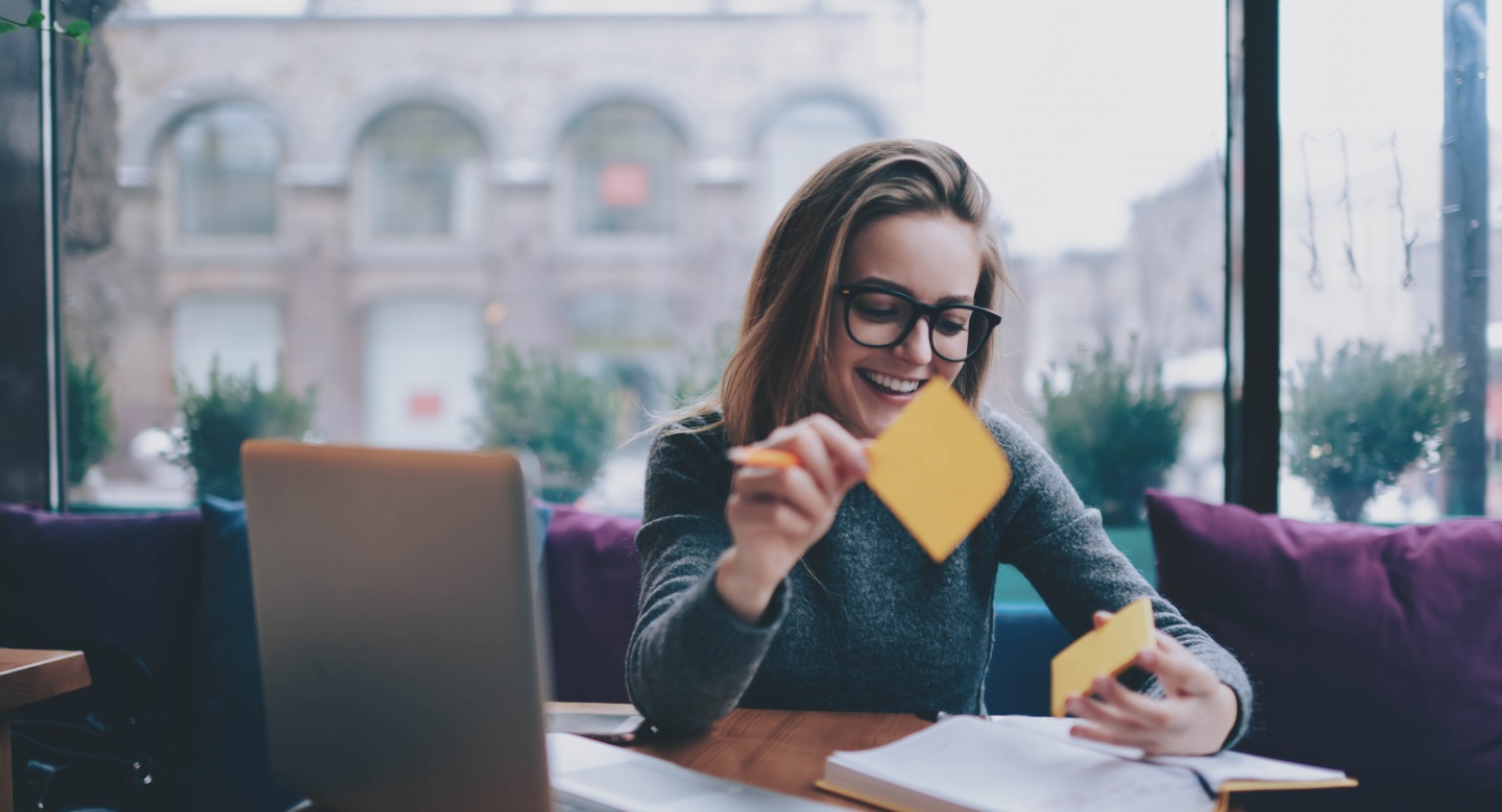 Женщина счастлива и улыбается, работая за ноутбуком в очках, глядя в камеру.