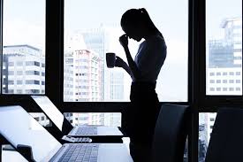 Человек сидит за столом в помещении, на фоне мебели.