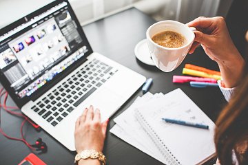 Ноутбук на столе с чашкой кофе, ручкой и клавиатурой компьютера.