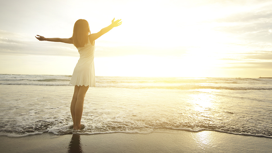 Женщина в пляжной одежде улыбается на фоне неба и природы.