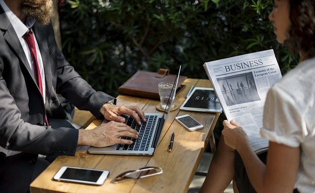 Мобильный телефон на столе с чашкой, ручкой; мужчина в галстуке читает текст.