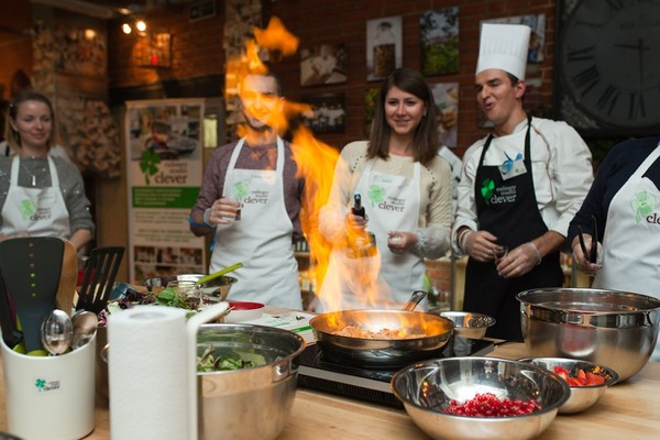 Женщина-повар в шляпе и мужчина-повар за столом с кастрюлей в стуле.