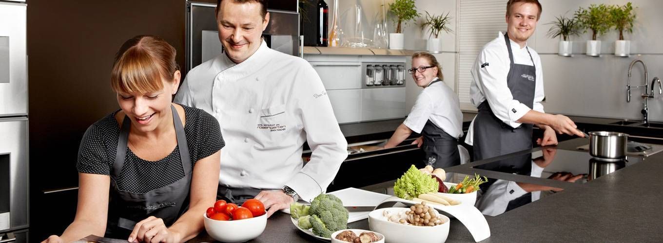 Женщина-повар с серьезным выражением лица, мужчина с гарнитуром на голове.