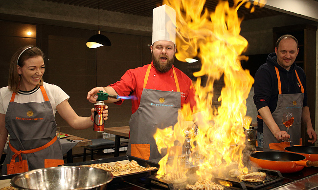 Повар в мужском кокошнике готовит на открытом огне в кастрюле.