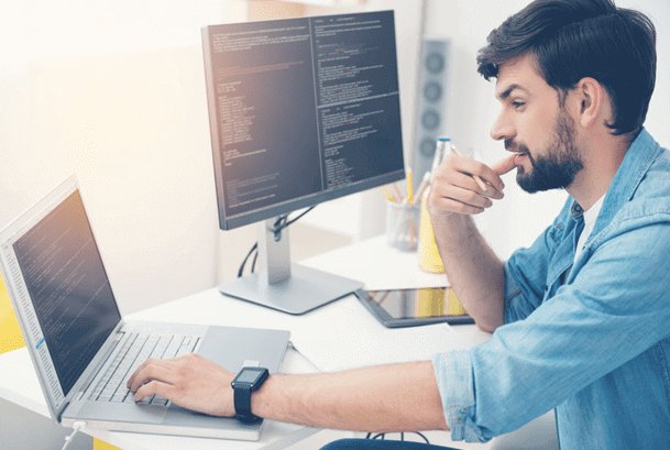 Взрослый мужчина сидит за столом с ноутбуком и мобильным телефоном.