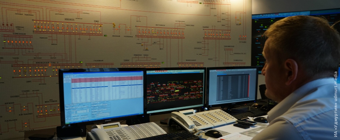 Человек сидит за столом перед монитором на фоне компьютерной клавиатуры.