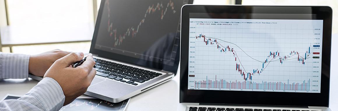 Ноутбук на столе с монитором, клавиатурой, экраном, диаграммой и другой компьютерной техникой.