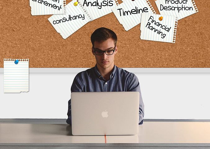 Человек сидит за столом с ноутбуком и компьютером на фоне мебели.