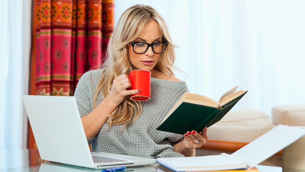 Человек читает с кружкой, компьютером. Личное использование ноутбука на столе.