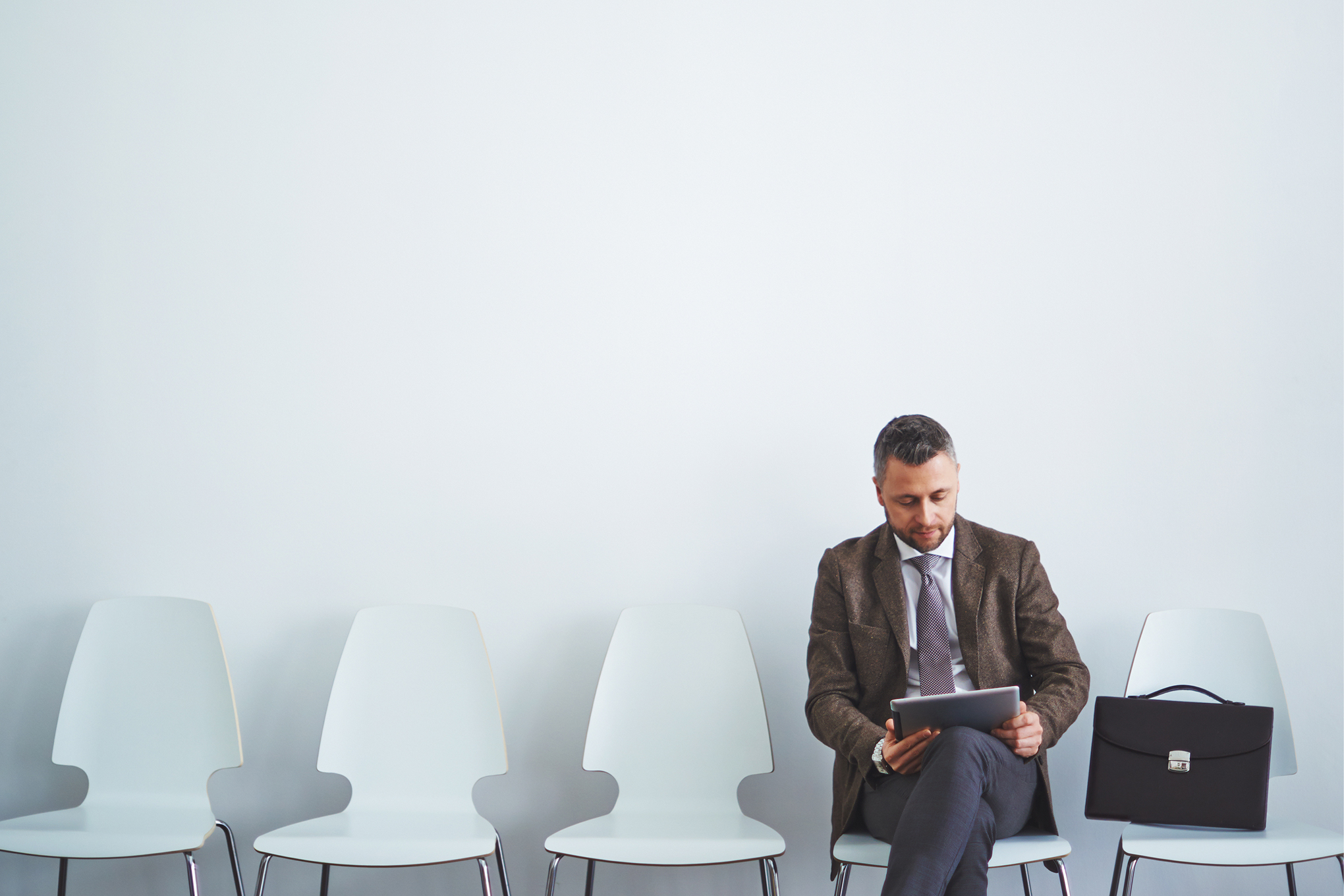 Мужчина сидит на стуле с ридерской сумкой, читает на компьютере.