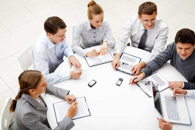 Люди разговаривают у компьютера с ноутбуком и клавиатурой. Hardware на фоне.