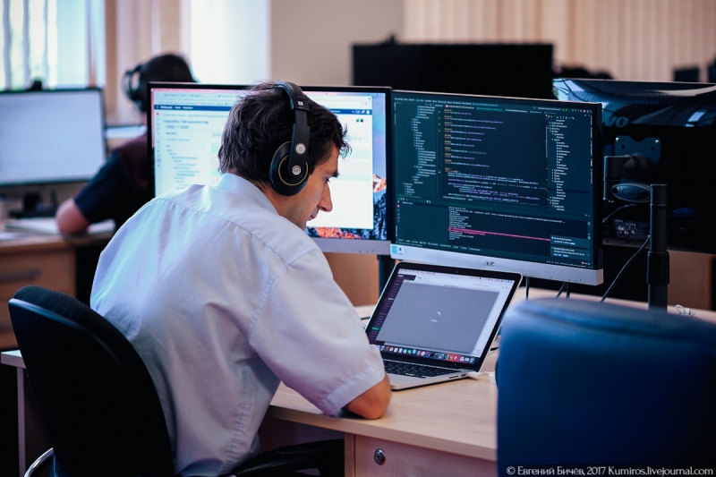 На столе компьютерные принадлежности: наушники, монитор, ноутбук, персональный компьютер.