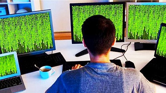 Человек играет в видеоигры на ноутбуке перед черной доской с чашкой кофе.